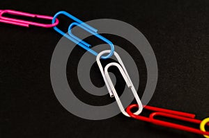 Many colorful paper clips lie on a black background paper