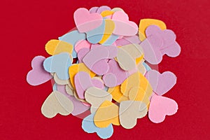 Many colorful paper heart shaped confetti on pink or red background. Valentine`s concept card
