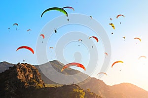 Many colorful paragliders in the blue sky over the mountains at sunset.