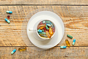 Many colorful pills in cup on wodden table