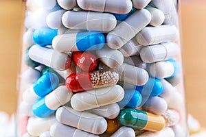 Many colorful pills in transparent glass on wooden background