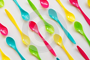 Many colorful plastic spoons on white background, top view