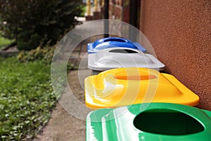 Many colorful recycling bins near brown wall outdoors, closeup. Space for text