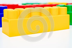 Many colorful toy plastic bricks, kit of blocks for building and constructing with a yellow one close up on white background with