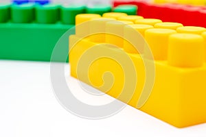 Many colorful toy plastic bricks, kit of blocks for building and constructing with a yellow one close up on white background with