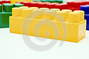 Many colorful toy plastic bricks, kit of blocks for building and constructing with a yellow one close up on white background with