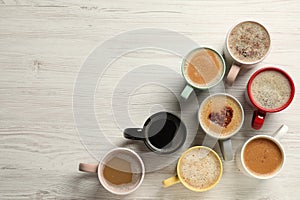 Many cups with different aromatic coffee on white wooden table, flat lay. Space for text