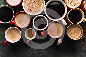 Many cups of different coffees on slate table, flat lay