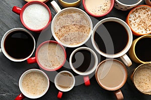 Many cups of different coffees on slate table, flat lay