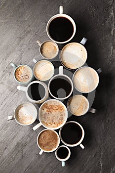 Many cups of different coffees on slate table, flat lay