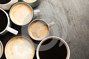 Many cups of different coffees on slate table, flat lay. Space for text