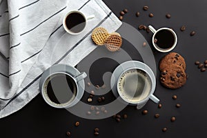 Many cups with tasty aromatic coffee and cookies on black background, flat lay