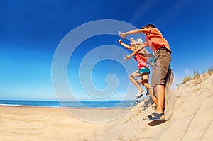 Many cute children jump from sand dune hands up