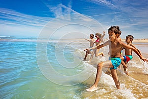 Many cute kids run to ocean waves on a beach