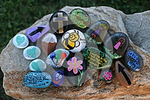 Many decorated painted rocks displayed on a small boulder