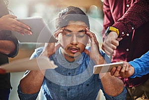 So many demands are bringing him down. Shot of a stressed out designer surrounded by demanding colleagues while sitting photo