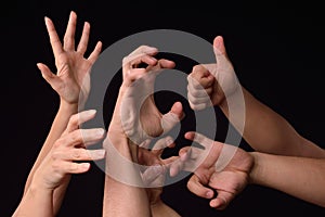 Many desperate female and male hands elevated into the air trying to reach or grab something on a black background