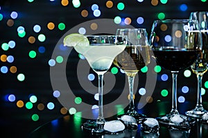 Many different alcoholic drinks on table against dark background with blurred lights