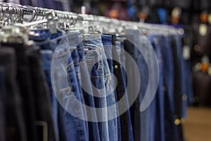 Many different blue Jeans on a hanging rack in the clothes shop store