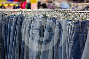 Many different blue Jeans on a hanging rack in the clothes shop store