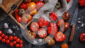 Many different breeds, shapes and sizes of tomatoes in an old wooden box and on a dark surface, flat lay