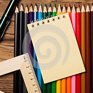 Many different colored pencils and empty notebook on wooden table