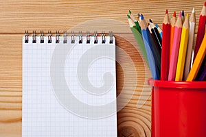 Many different colored pencils and empty notebook on wooden table