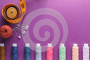 Many different colorful sewing threads and a measuring tape on a purple background