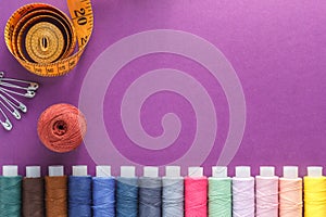 Many different colorful sewing threads and a measuring tape on a purple background