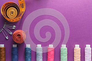 Many different colorful sewing threads and a measuring tape on a purple background