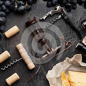 Many different corkscrews with open wine corks on dark concrete background in frame made of black grapes. Degustation