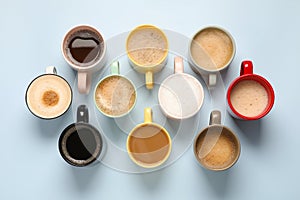 Many different cups with aromatic coffee on light blue table, flat lay