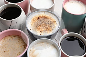 Many different cups with aromatic hot coffee on white wooden table, closeup