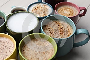 Many different cups with aromatic hot coffee on white wooden table, closeup