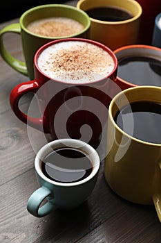 Many different cups with aromatic hot coffee on wooden table