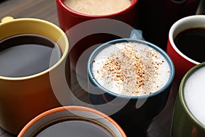 Many different cups with aromatic hot coffee on wooden table, closeup
