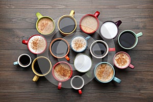 Many different cups with aromatic hot coffee on wooden table, flat lay