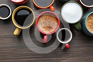 Many different cups with aromatic hot coffee on wooden table, flat lay