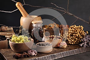 Many different dry herbs, flowers and mortar with pestle on black table