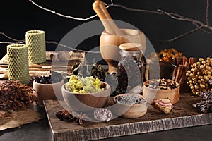 Many different dry herbs, flowers and mortar with pestle on dark grey table