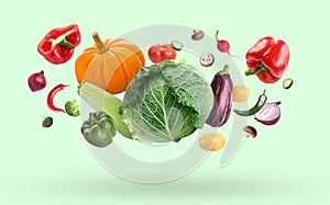 Many different fresh vegetables falling on pale light green background