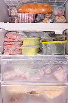 Many different frozen raw food in containers in a home freezer, meat, vegetamles, bread and semies, kitchen home