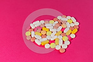 Many different pills and tablets folded in shape of heart on pink background.