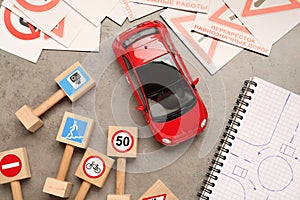 Many different road signs, notebook with sketch of roundabout and toy car on grey table, flat lay. Driving school