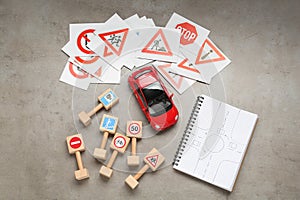 Many different road signs, notebook with sketch of roundabout and toy car on grey table, flat lay. Driving school