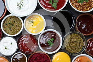Many different sauces and herbs on black table, flat lay