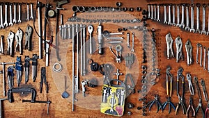 Many different sizes of tools, wrenches and pliers hanging on wooden panel background.