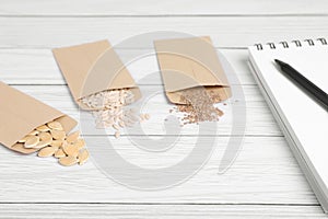 Many different vegetable seeds and notebook on white wooden table