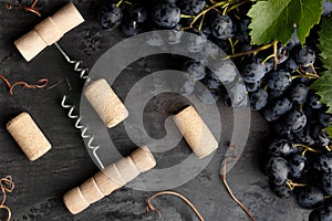 Many different wooden corkscrews with open wine corks on dark concrete background in frame made of black grapes