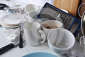 Many dirty utensils and dishware on countertop in messy kitchen